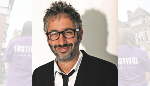 Studio portrait of a person wearing glasses and a suit against a plain light background.