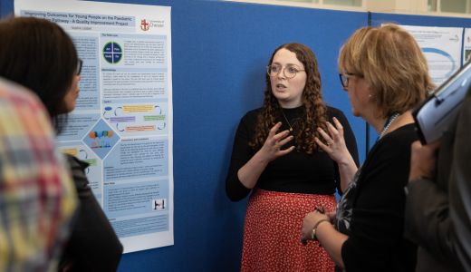 Person presenting a research poster to a small group in an indoor exhibition setting with display boards.