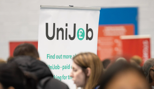 Crowded indoor event with a “UniJob” banner promoting paid work for students, with attendees in the foreground.
