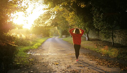 Woman walking down a road lined with trees in the sun
