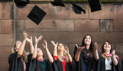 A group of graduates in gowns celebrate together by throwing their mortarboards into the air .