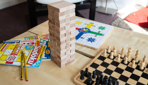 A table displaying a chess set, a board game, and puzzle magazines with pencils.