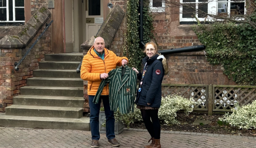 Two people stand outside a brick building, holding up a green striped jacket between them.
