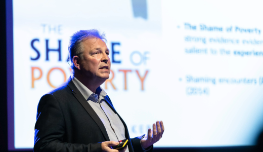 Professor Paul Bissell on stage in front of a large screen. 