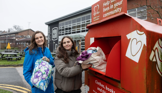 Two people donate clothes into a British Heart Foundation collection bin.