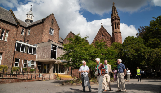 A group of visitors walking through a courtyard area surrounded by red‑brick historic buildings and a tower.