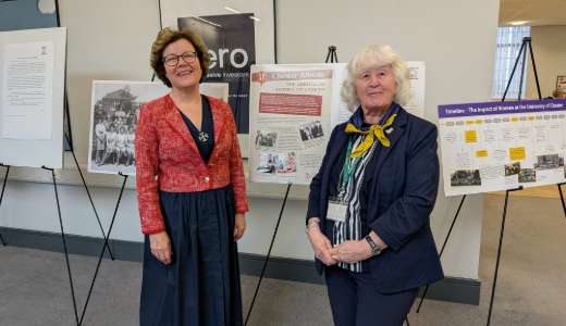 Two people posing in front of exhibition boards showing historical information and photographs.