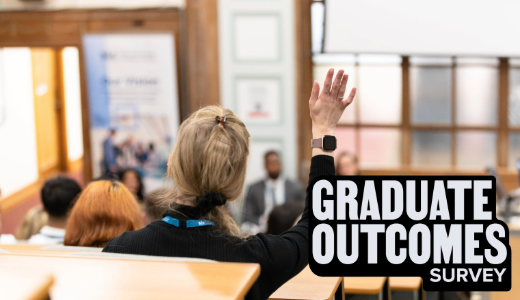 A person raising a hand in a lecture room, with “Graduate Outcomes Survey” displayed prominently on screen.