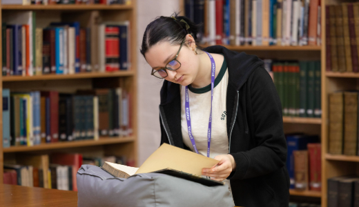 A person examining a historical document in a library with bookshelves in the background.