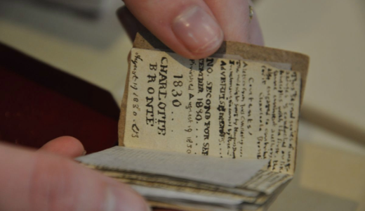 Close-up of hands holding a very small, worn booklet with printed historical text inside.