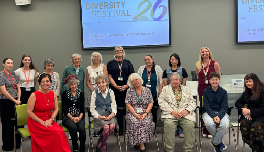 Group of staff, students and guests posing for a photograph at a Diversity Festival event, with presentation screens visible in the background.