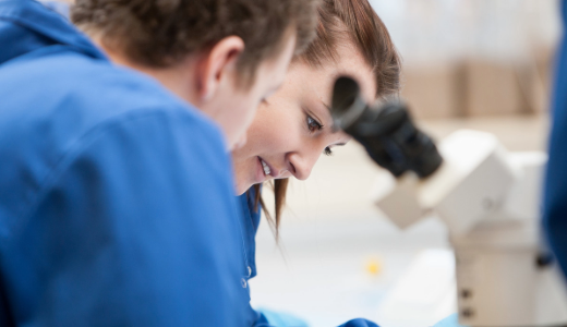 Students working in a laboratory, with a microscope visible in the foreground.