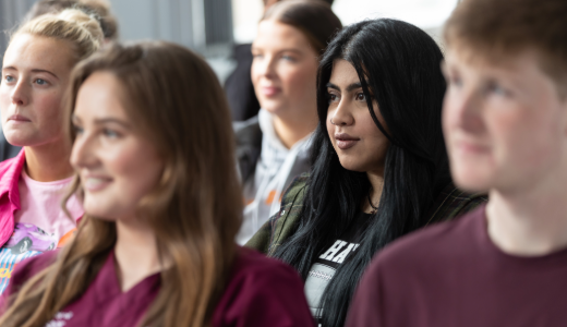 Students seated in a classroom or lecture setting, listening to a presentation or discussion.