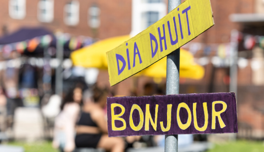 Signpost displaying greetings in different languages at an outdoor community event.