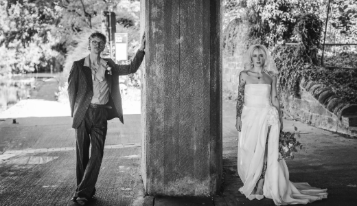 Black and white wedding portrait of two people standing on either side of a concrete pillar beneath a bridge.