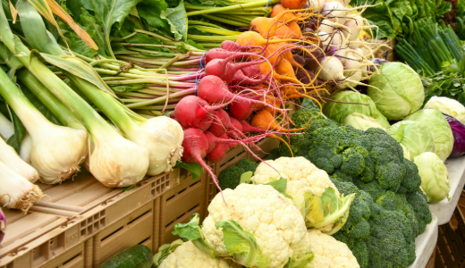 Selection of fresh vegetables, including onions, radishes, carrots, cabbages, cauliflower and broccoli, displayed at a market stall.