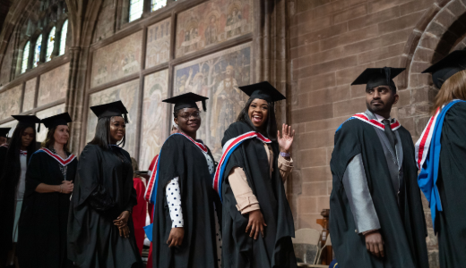 Graduates in academic gowns and mortarboards walking through a historic hall during a graduation ceremony.
